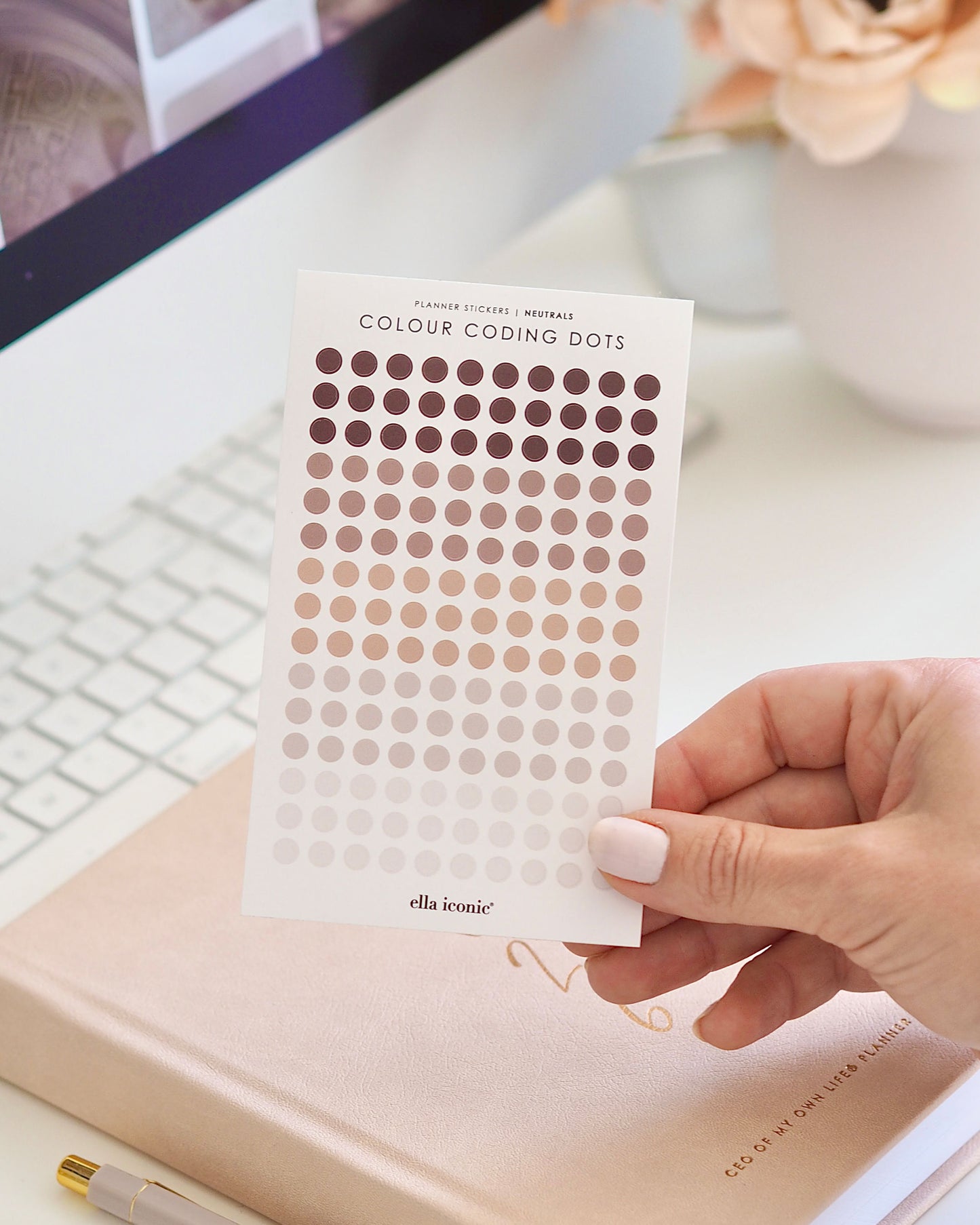 Hand holding a sheet of Colour Coding Dots by ella iconic on a desk with a keyboard and notebook.